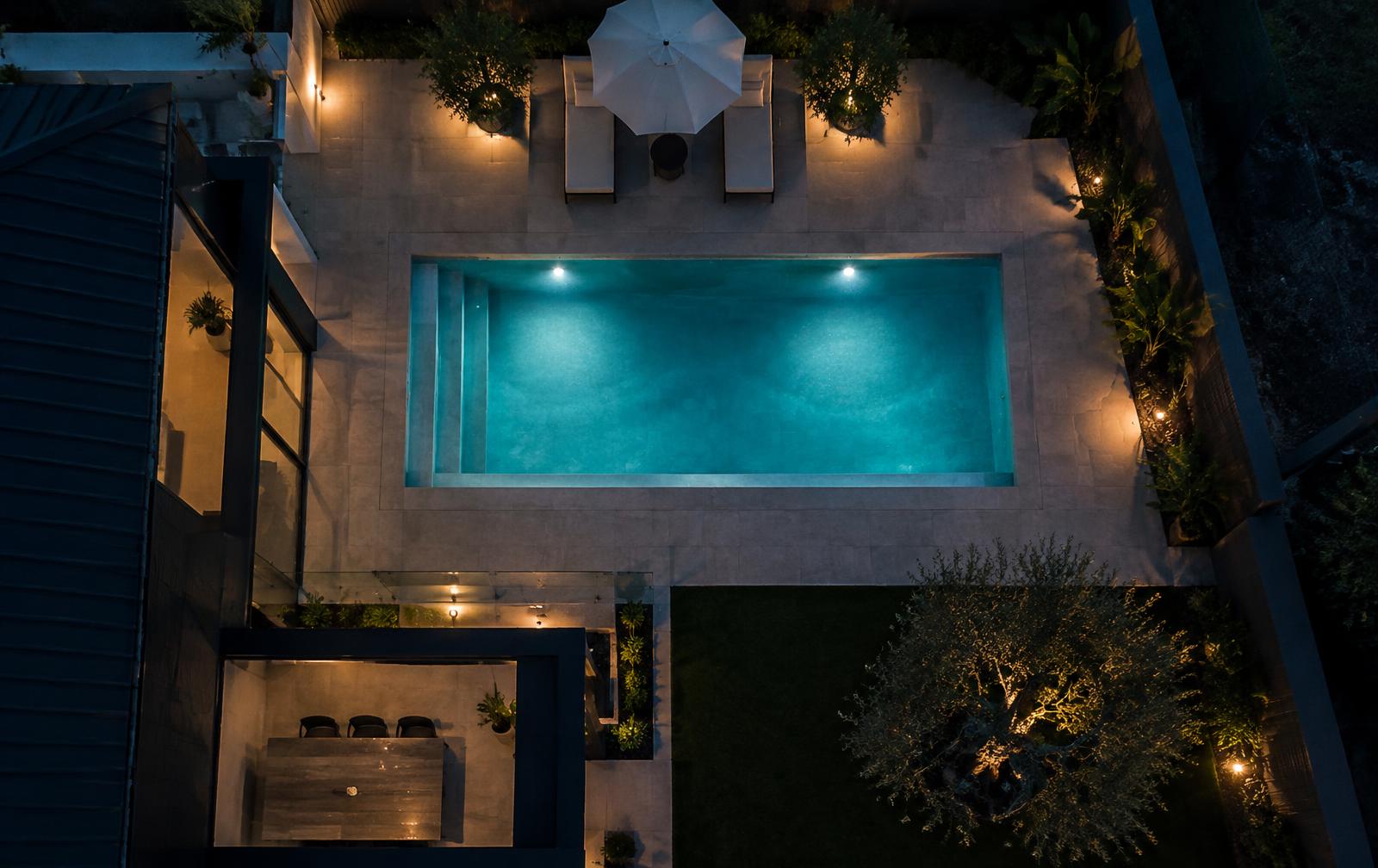 Aerial view of a lit backyard pool at dusk